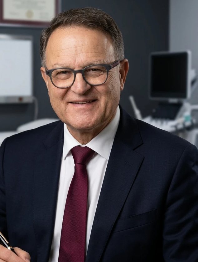 Dr Assan Maghsoudlou, Senior Orthopaedic Surgeon, smiling in a suit and burgundy tie